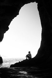 Silhouette man on rock by sea against clear sky