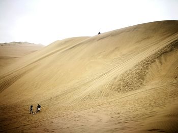 People walking on sand dune against clear sky