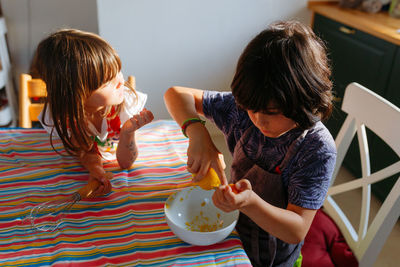 Two girls sitting at the table preparing cake in the kitchen at home