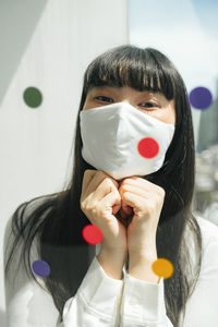 Portrait of woman wearing mask sitting by window at home