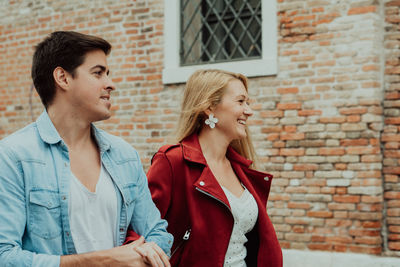 Portrait of a smiling young woman standing against brick wall