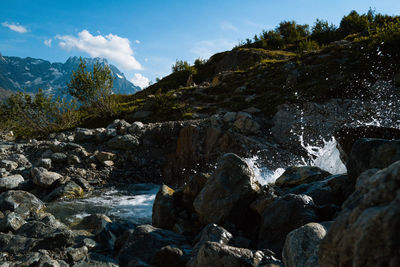 Stream flowing through rocks against sky