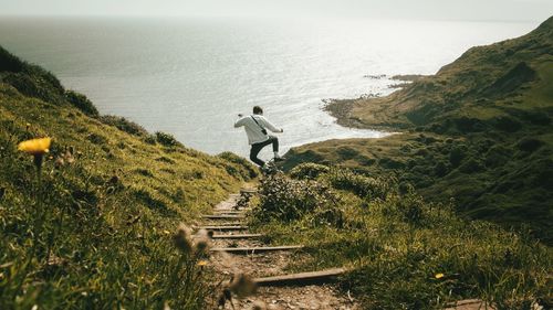 Rear view of man jumping on mountain by sea