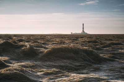 Lighthouse on field by building against sky