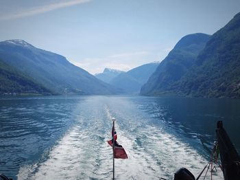 Norwegian flag waving in the wake of a fjord boat with a panoramic view of sognefjord.