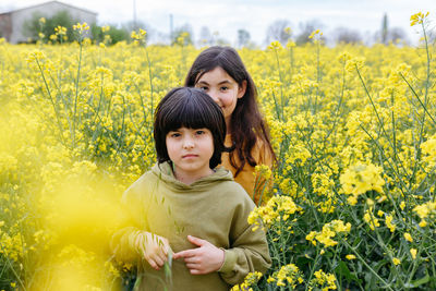 Two happy standing girls hugging each other in the field with yellow flowers