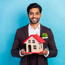Portrait of man holding model house against blue background