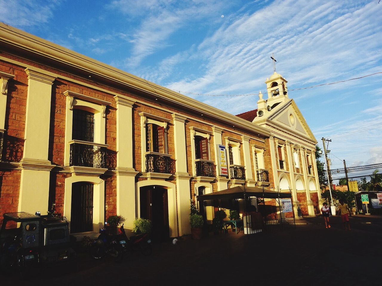 architecture, building exterior, built structure, sky, street, low angle view, church, facade, city, window, religion, place of worship, cloud - sky, building, cloud, incidental people, outdoors, travel destinations, car, transportation