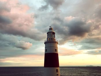 Lighthouse by sea against sky during sunset