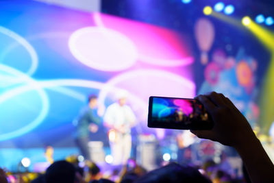 Reflection of hand on illuminated smart phone at music concert