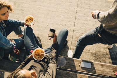 High angle view of teenage boy using smart phone while eating meal with friends on street in city