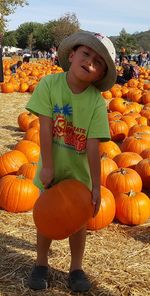Full length of boy standing by pumpkin on field during autumn