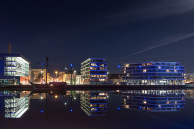 Illuminated buildings by river against sky in city at night