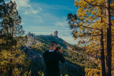 Rear view of man photographing mountains against blue sky