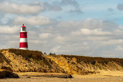 Lighthouse on land by building against sky