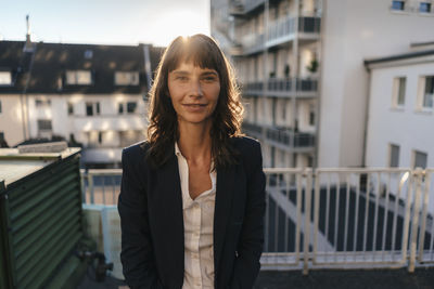 Portrait of smiling woman standing against railing in city