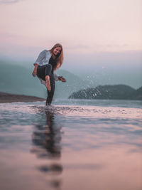 Full length of woman in sea against sky during sunset