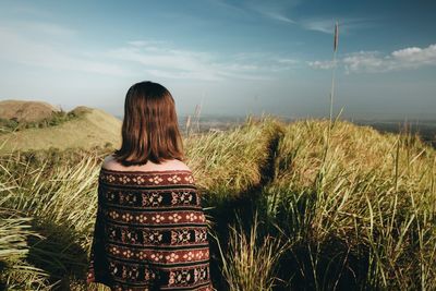 Rear view of girl standing at grassy field against sky