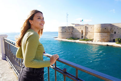 Portrait of smiling relaxed traveler woman looking taranto city from seafront, apulia, italy