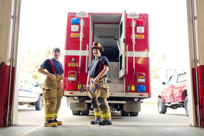 Portrait of happy fire fighters standing against fire engine