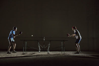 Male friends playing table tennis against building