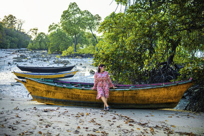 Rear view of boy standing on boat against trees
