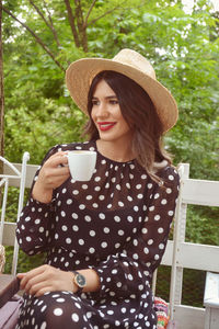 Smiling young woman drinking coffee while sitting at porch 