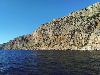 Scenic view of sea and mountains against clear blue sky