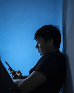 Side view of young man using phone at home