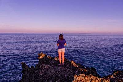 Rear view of woman standing on rock formation against horizon