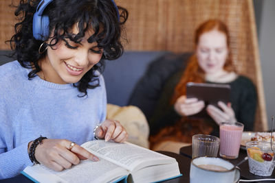 Young woman with dark curly hair with headphones reading book