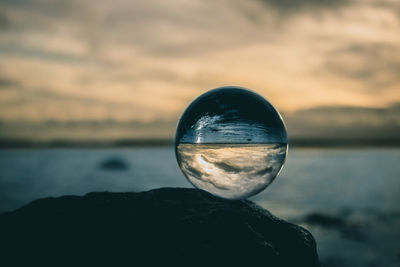 Close-up of crystal ball on rock against sky during sunset