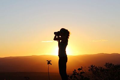 Silhouette of woman photographing at sunset