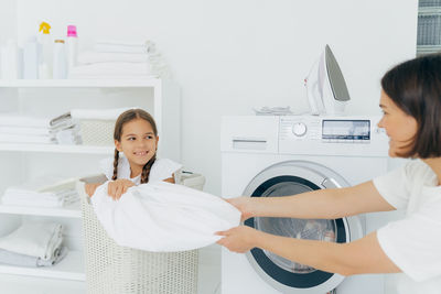 Playful mother with daughter doing laundry at home