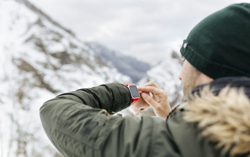Spain, asturias, young man using smartwatch in the snowy mountains