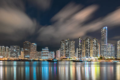 Illuminated city by sea against sky at night