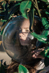 Close-up of young woman wearing glass ball on head amidst leaves