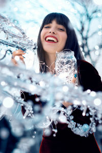 Portrait of smiling young woman holding jar with illuminated string light during christmas