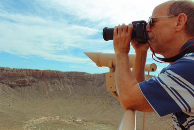 Side view of man photographing camera on landscape against sky