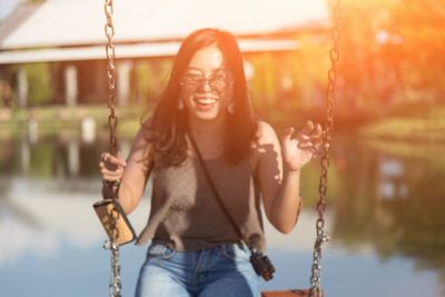 Portrait of smiling woman sitting on swing against lake