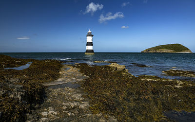 Lighthouse on beach by sea against sky