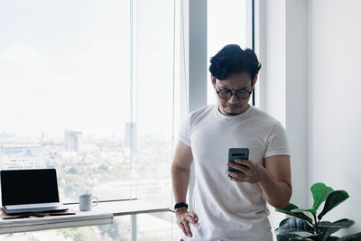 Young man using mobile phone while standing on window