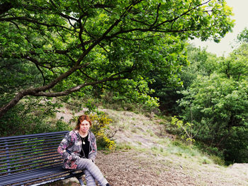 A caucasian girl is sitting on a bench in a park under an oak tree person