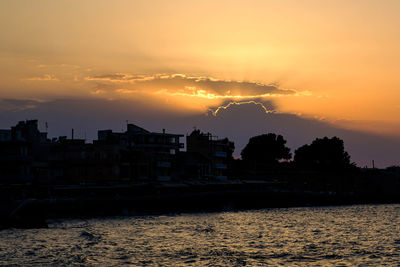 Silhouette buildings by sea against sky during sunset