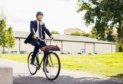 Full length of businessman riding bicycle on street against sky