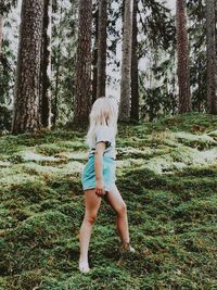 Full length of woman standing by tree trunk in forest