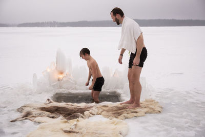 Side view of mature man looking at son taking ice bath at frozen lake
