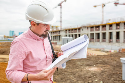 Midsection of man holding paper while standing at construction site