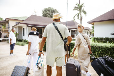 Rear view of family walking with luggage towards villa during vacation