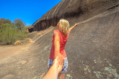 Rear view of women holding hand of man while standing against rock formation 